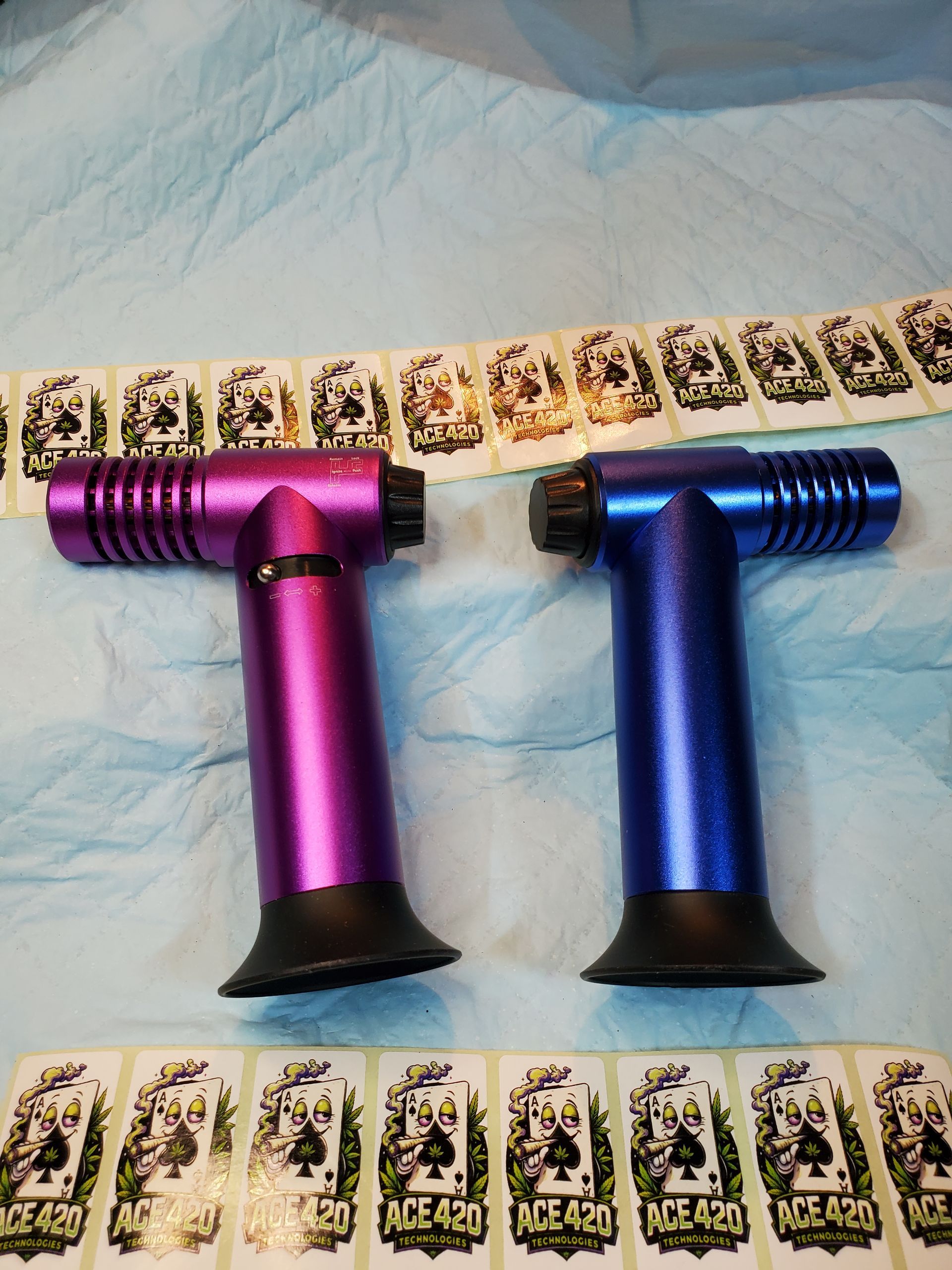 Two colorful metal T-shaped devices, one purple and one blue, laid on a blue cloth with card strips nearby