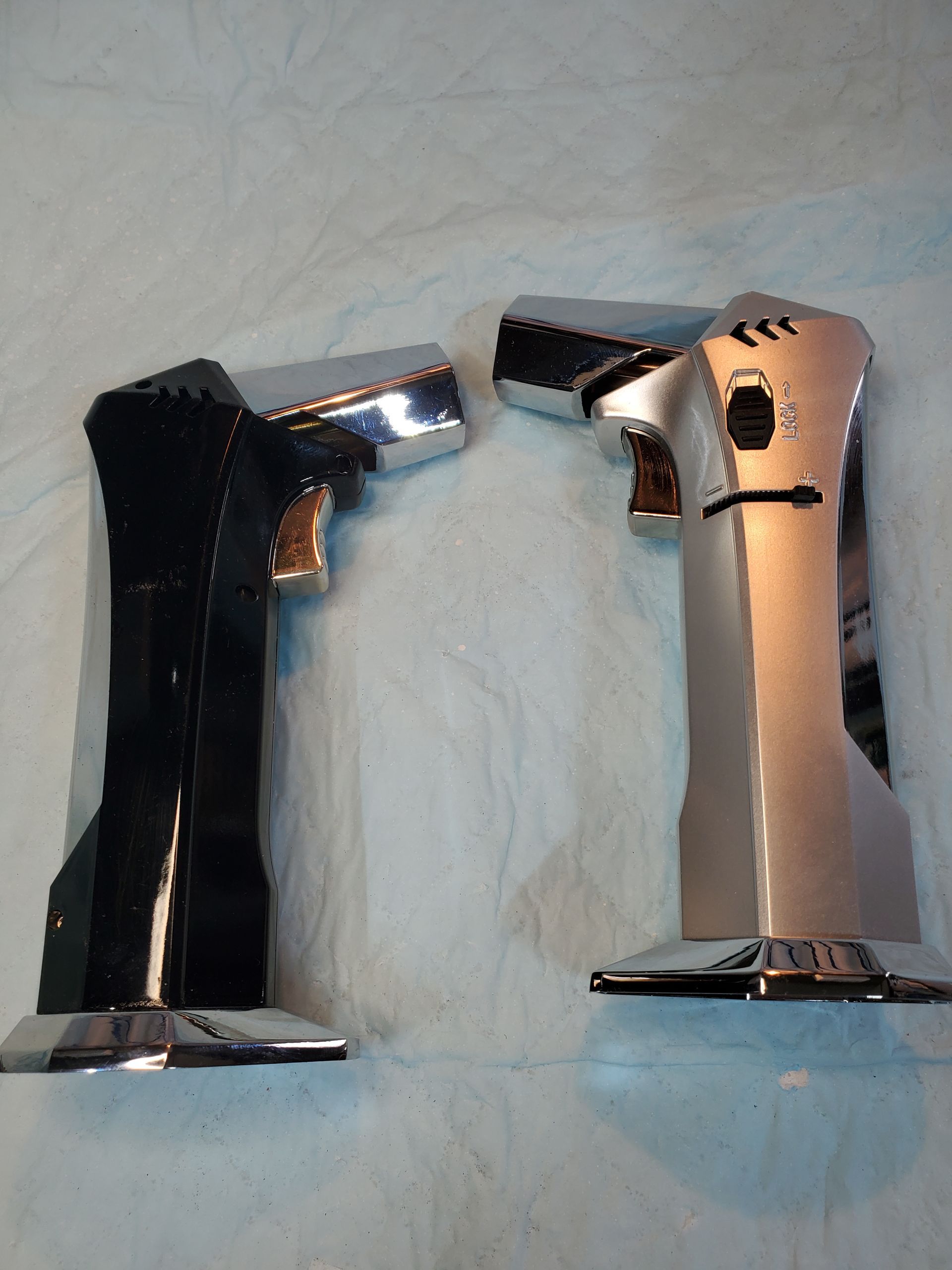 Two lighters, one black and one silver, standing upright on a light blue surface.