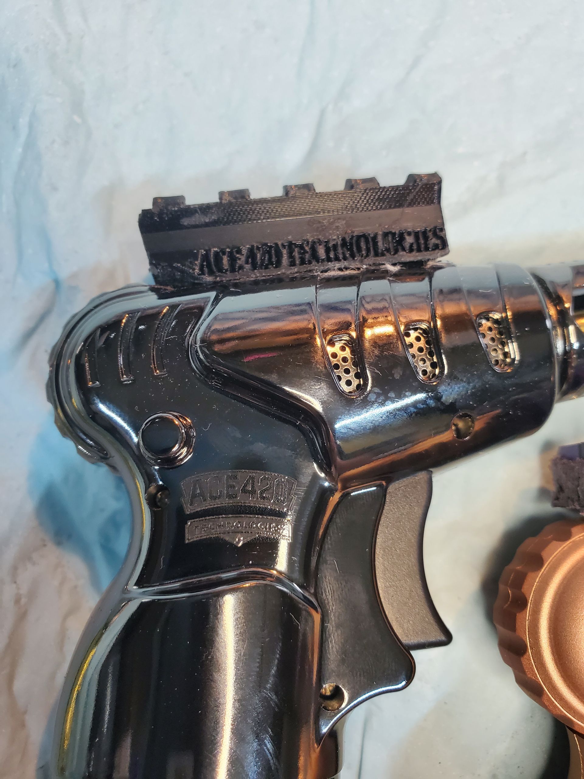 Red toy-style handgun with a black-and-gold Ace of Spades card and metallic cartridges on a white surface