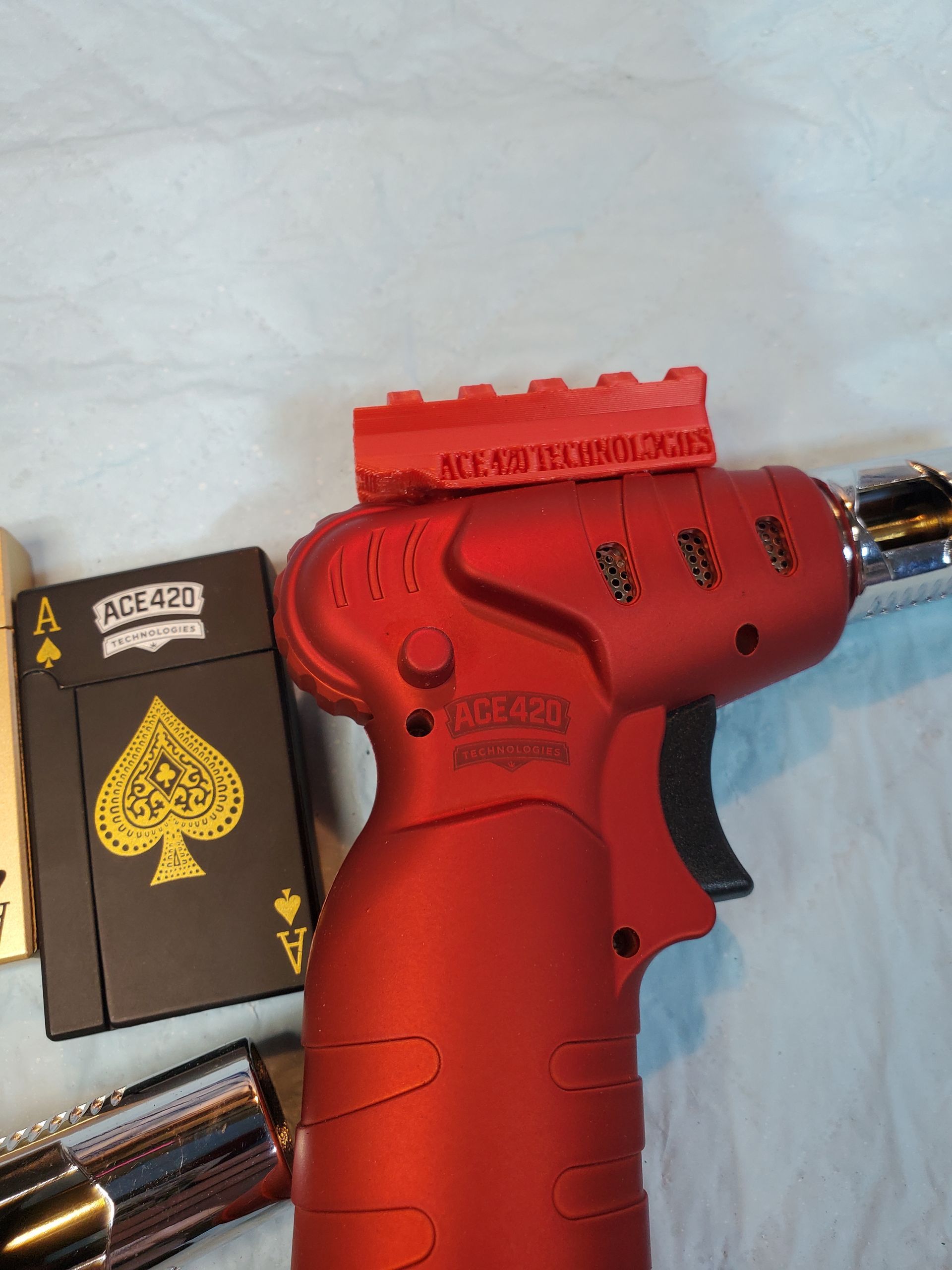 Red toy-style handgun with a black-and-gold Ace of Spades card and metallic cartridges on a white surface