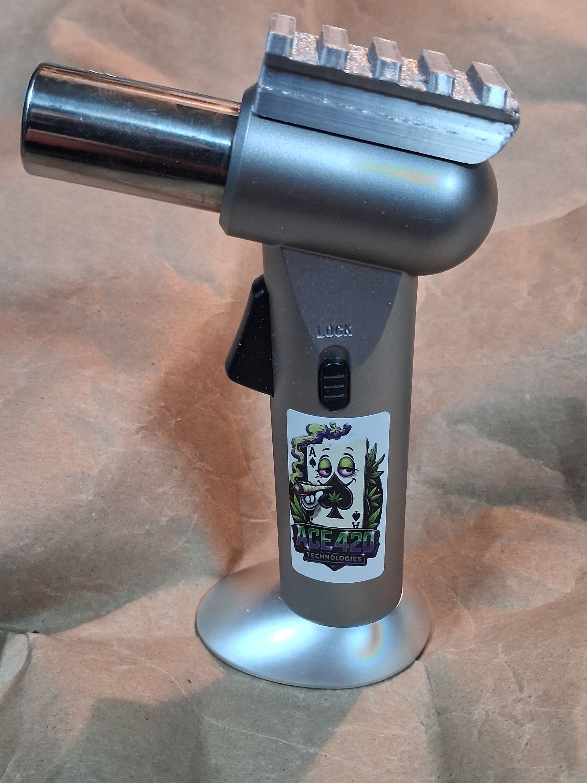 Silver butane torch lighter with black trigger and decorative label on a tan surface