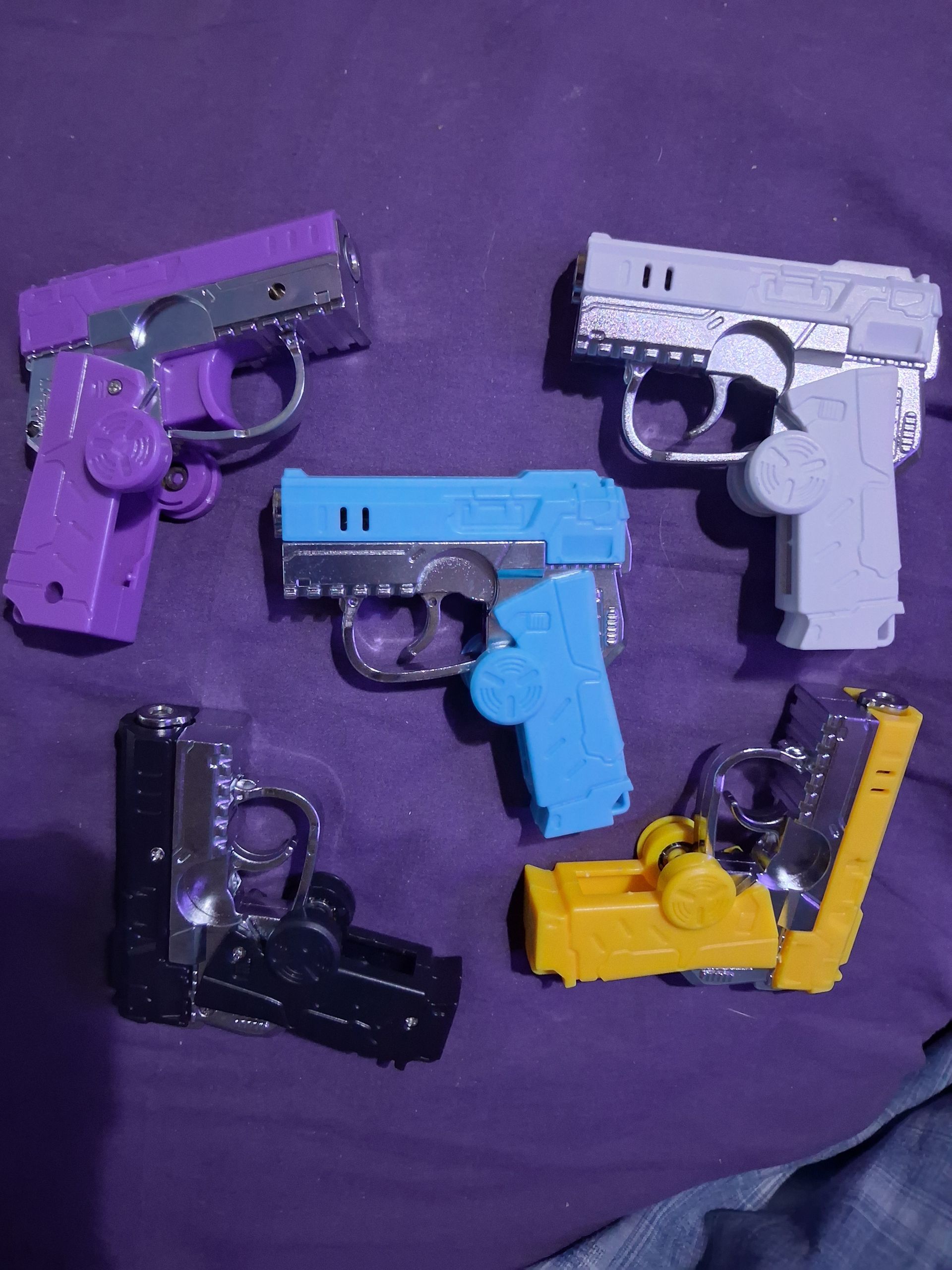 Five colorful toy pistols arranged on a purple fabric background.