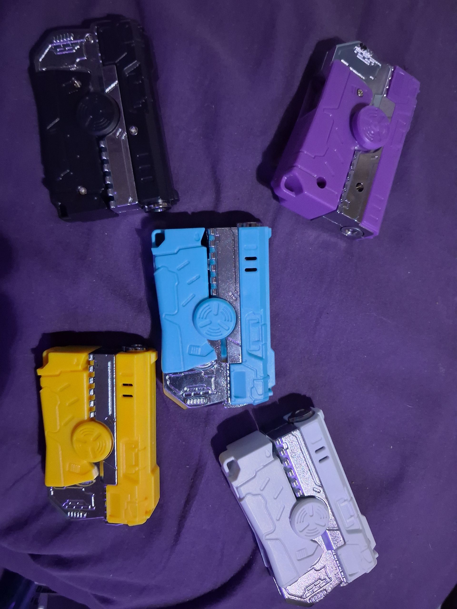 Five colorful toy pistols arranged on a purple fabric background.