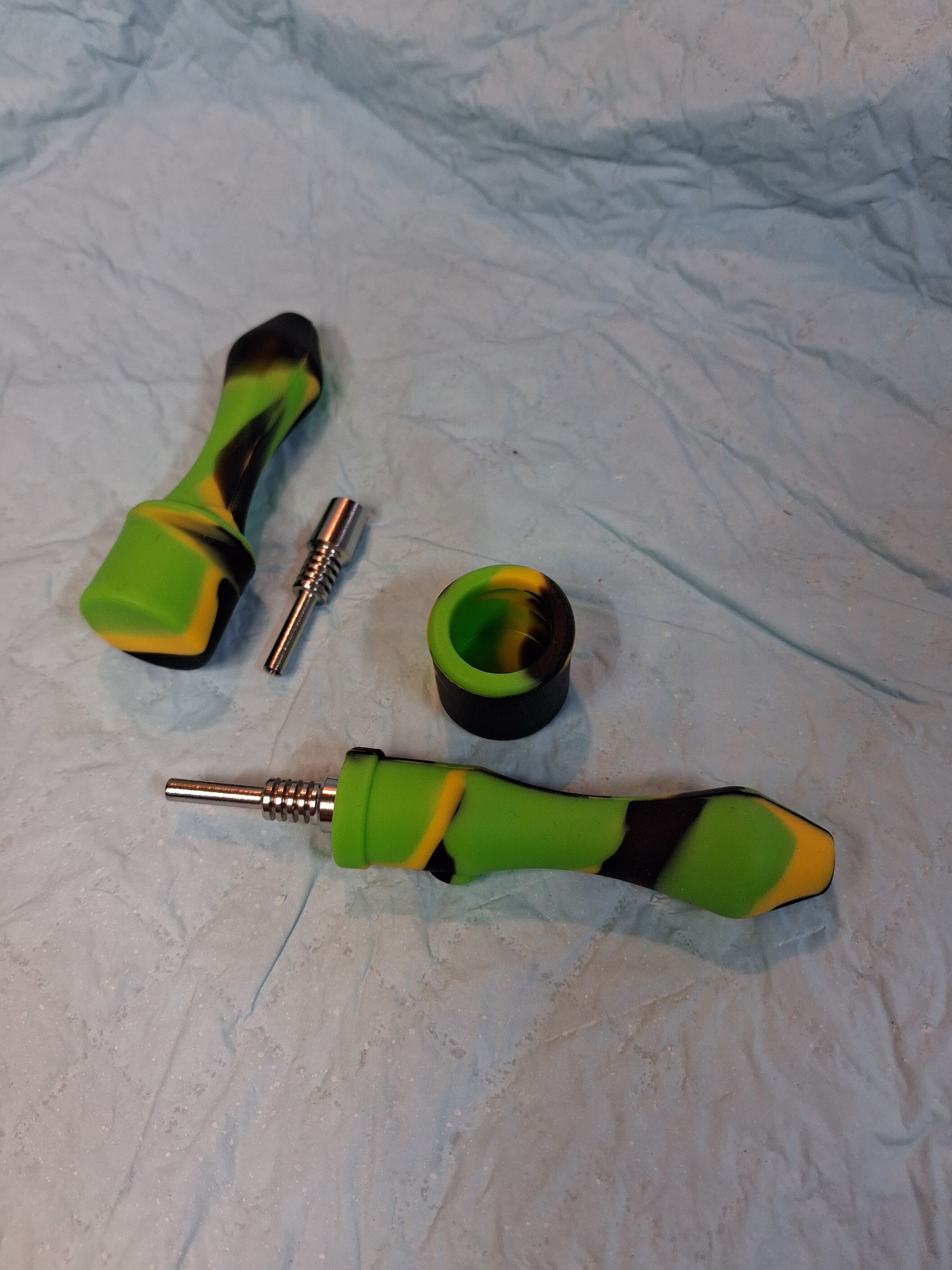 Green-and-black twisted earbuds with a silver connector and a matching round bead on a white cloth
