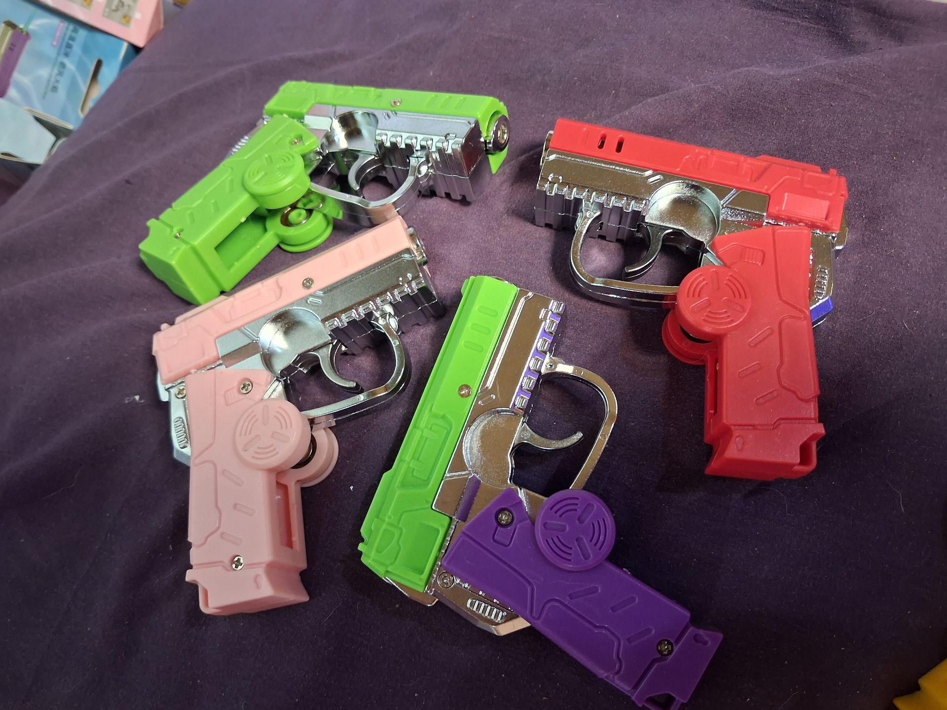 Six colorful toy plastic pistols arranged on a dark fabric surface.