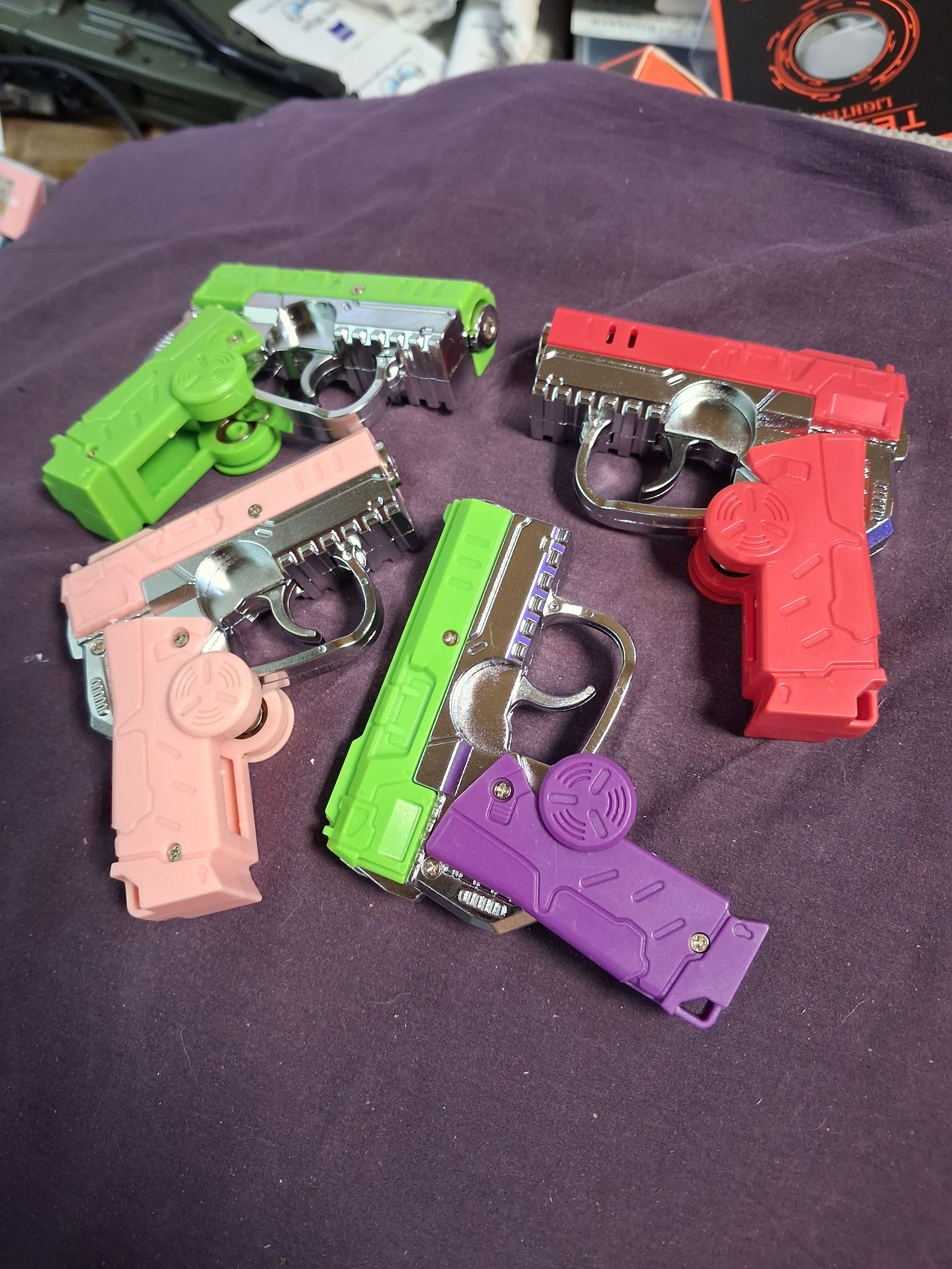 Six colorful toy plastic pistols arranged on a dark fabric surface.