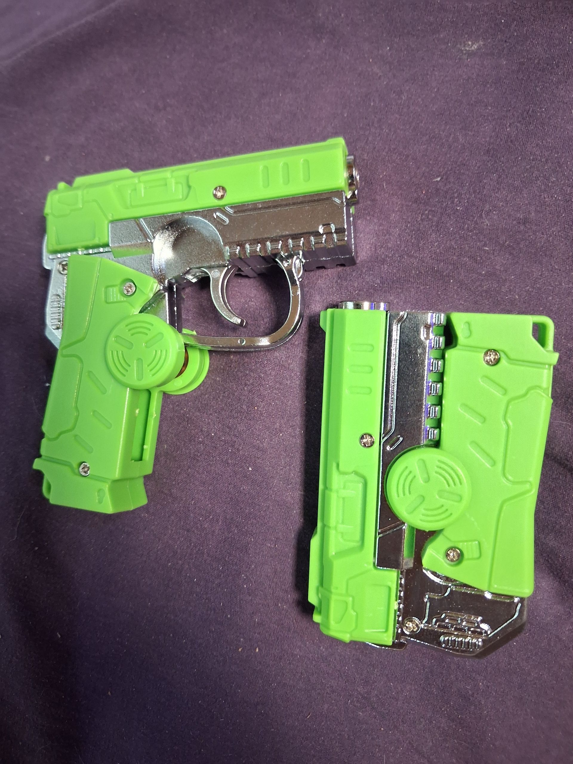 Two neon green toy pistols with black details on a purple cloth surface