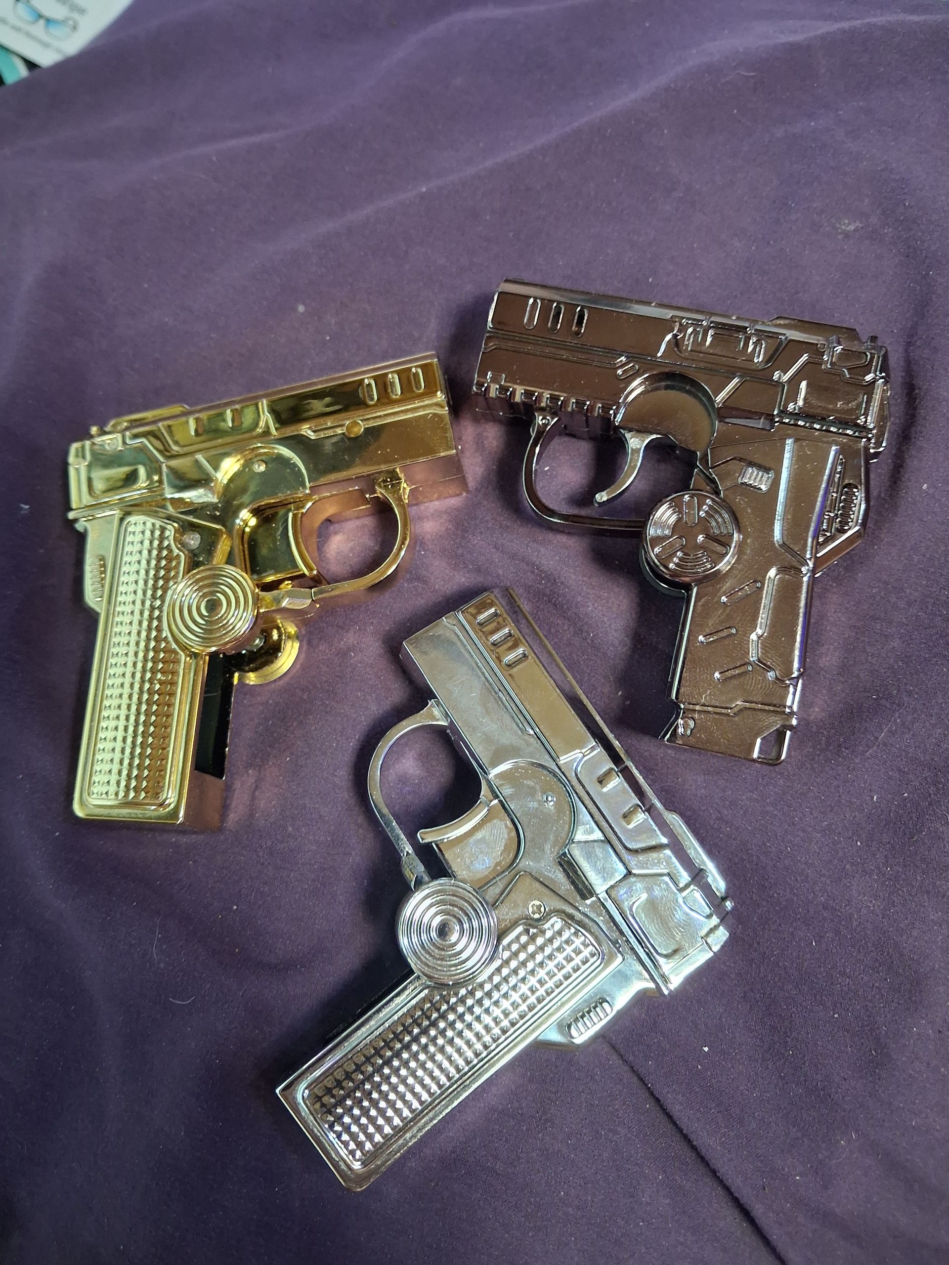 Three toy guns in gold, silver, and bronze on a purple cloth background