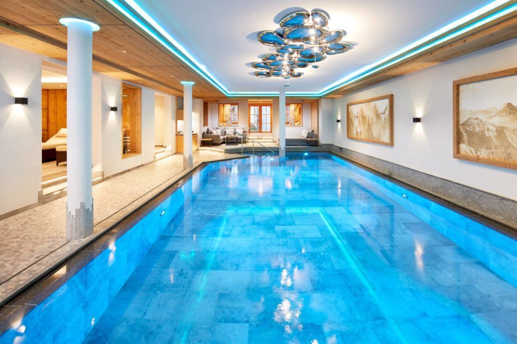 Ein großes Hallenbad mit einem Kronleuchter und edlen grauen Bodenfliesen.