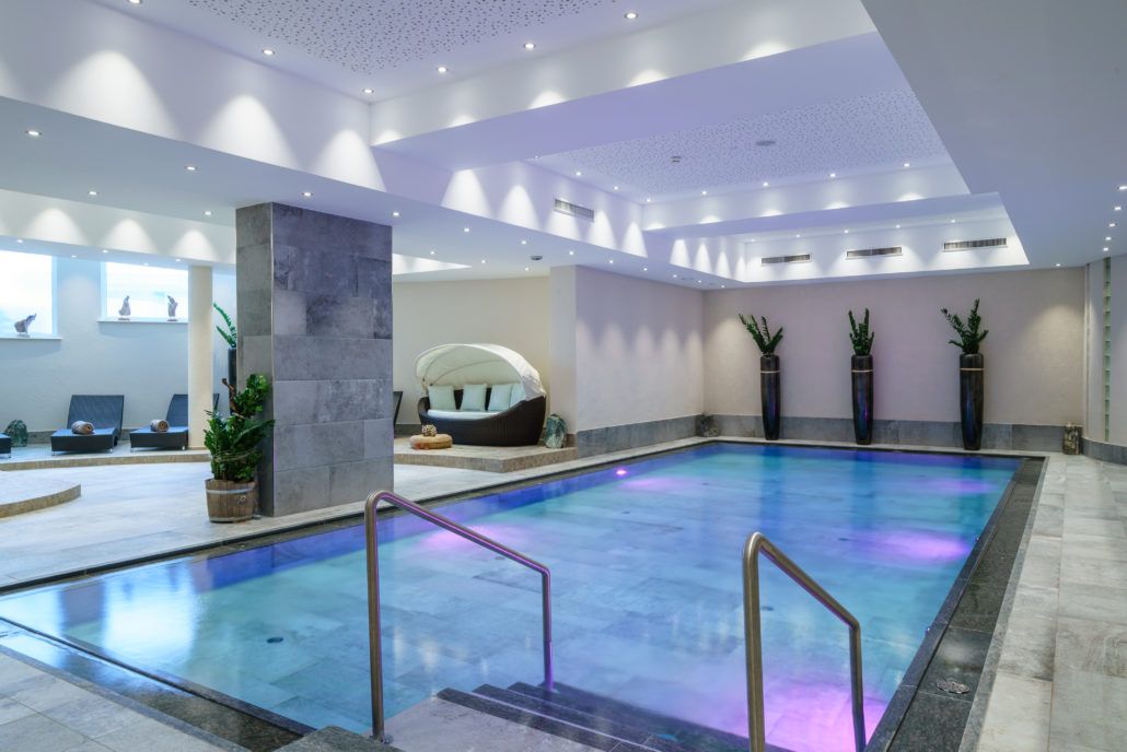 Ein großes Hallenbad mit Treppe in den Pool, der Boden ist aus edlen Fliesen.