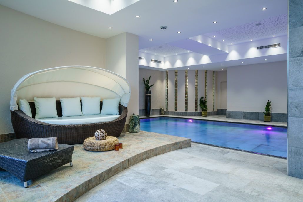 In der Mitte des Raumes befindet sich ein großer Swimmingpool, links befindet sich ein Loungebereich