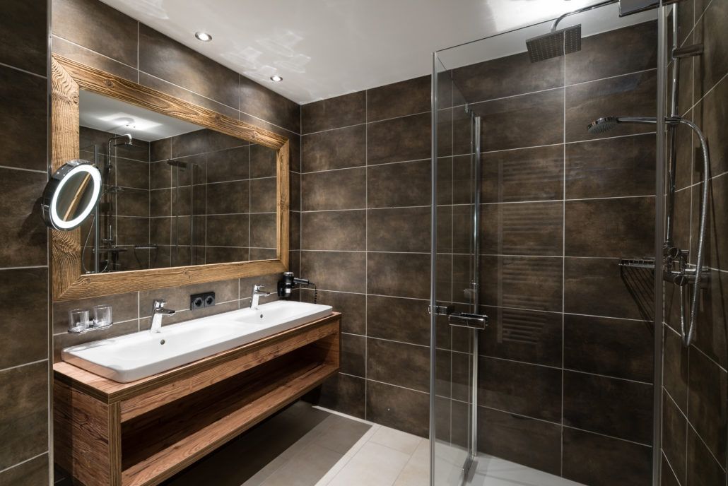 Ein Badezimmer mit grauen Wandfliesen, zwei Waschbecken und einer ebenerdigen Dusche.