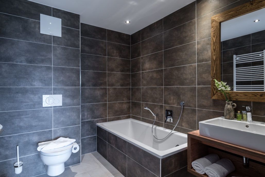 Ein Badezimmer mit Natursteinfliesen,  Badewanne, Toilette, Waschbecken und Spiegel.
