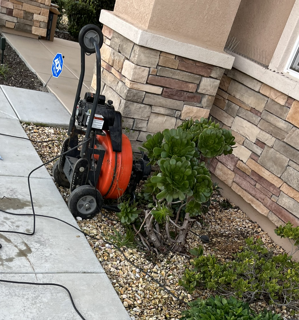 A drain cleaner is sitting on the sidewalk next to a brick building.