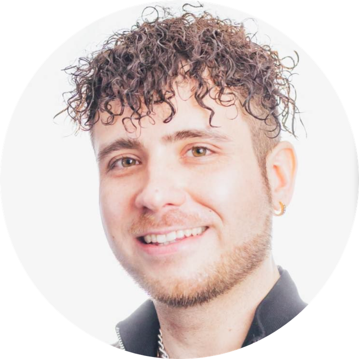 Man with curly hair smiling, wearing a black top and gold earring, set against a white backdrop.