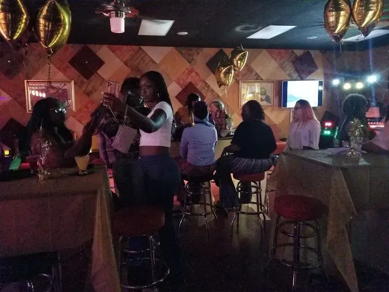 Dimly lit bar with people seated at tables and balloons hanging from the ceiling.