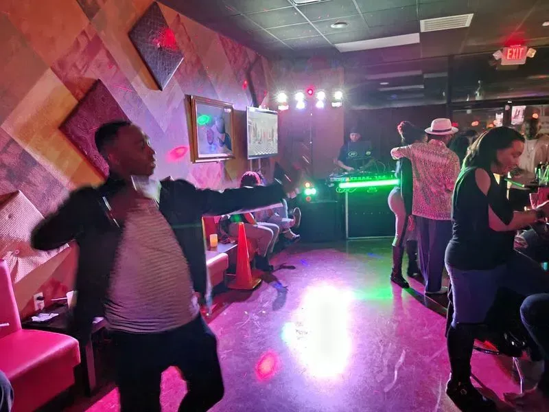 People dancing in a dim nightclub with colorful lights and a glowing DJ booth