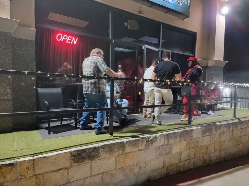 People standing on a restaurant patio at night, with an “OPEN” neon sign glowing inside.