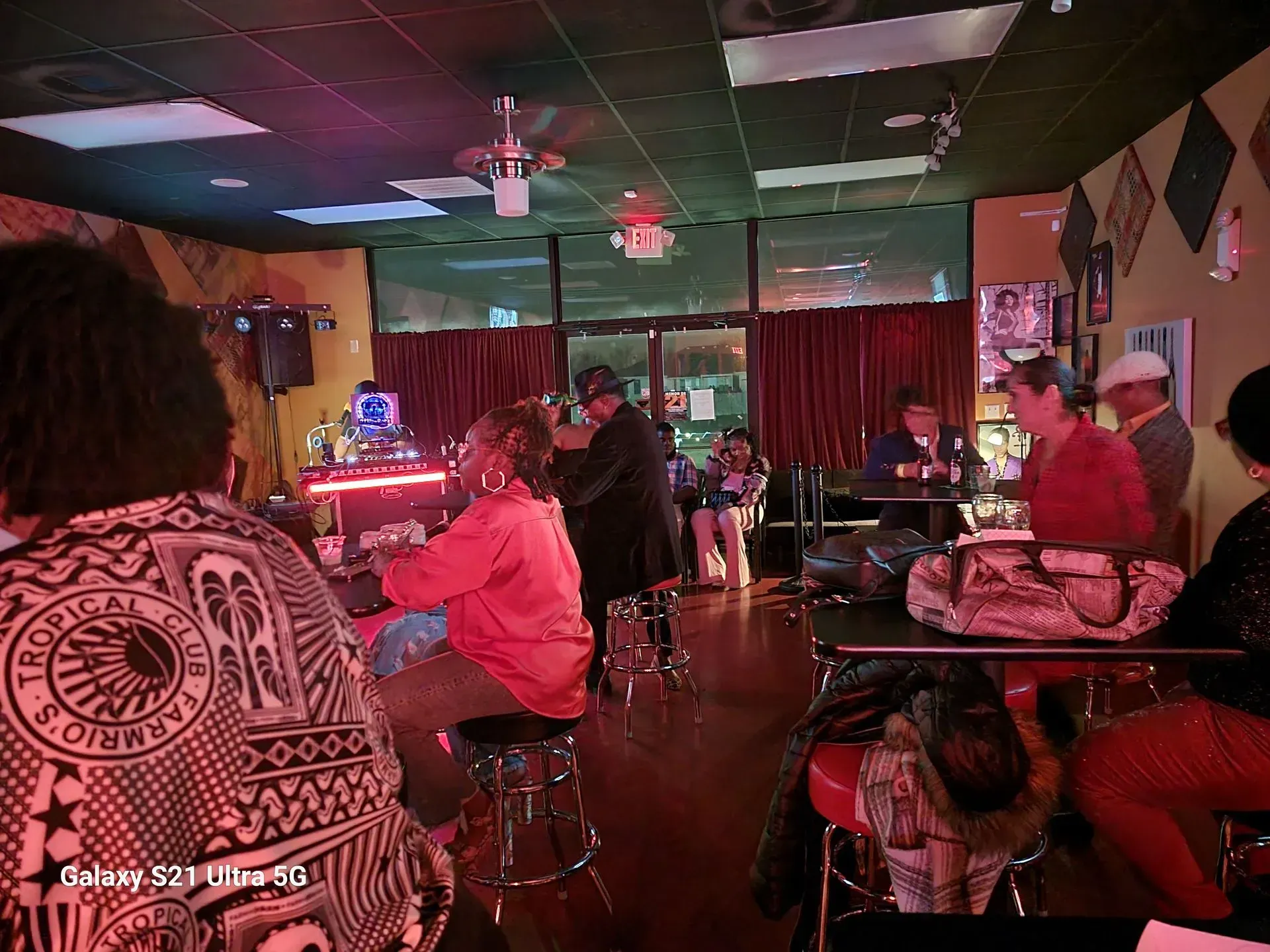 People seated at tables in a dimly lit lounge with red curtains and a stage area in the back
