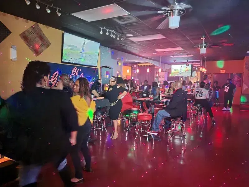Crowded neon-lit bar with people dancing and sitting at tables on a shiny floor