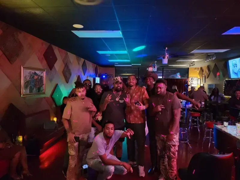 People posing in a neon-lit nightclub with colorful lights and drinks on a table