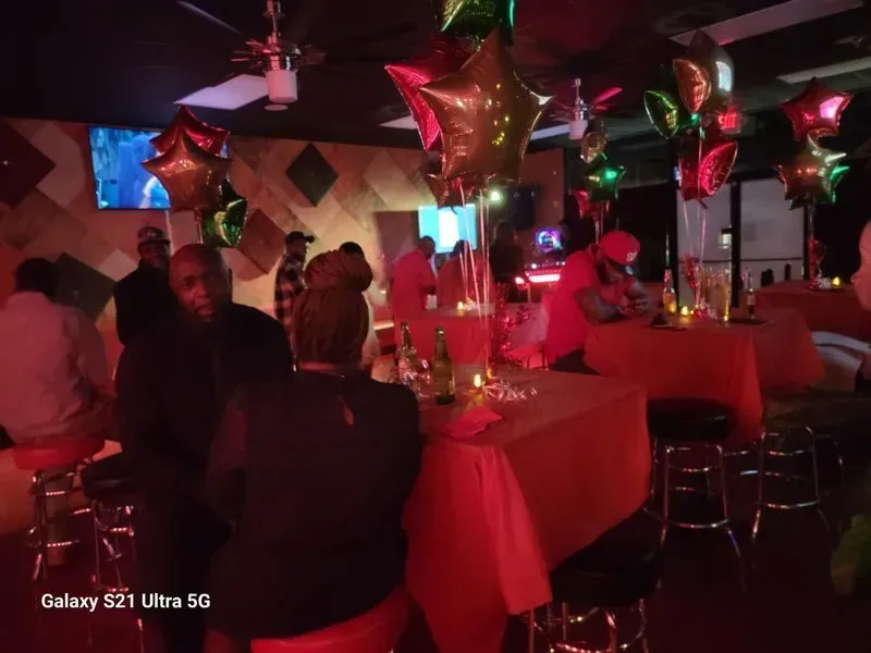 Dimly lit party room with red and green balloon decorations and tables set for guests