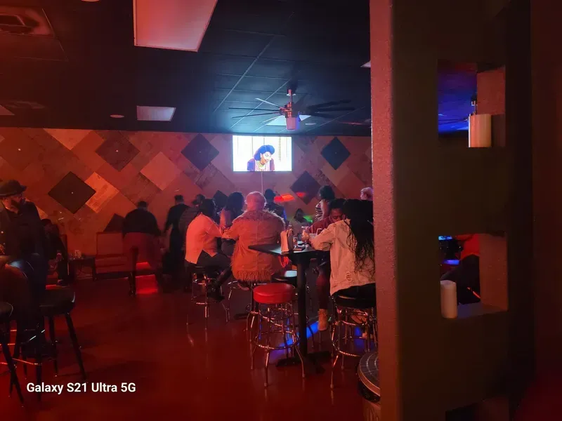 Dim bar with people seated at tables and a TV playing above the stage.