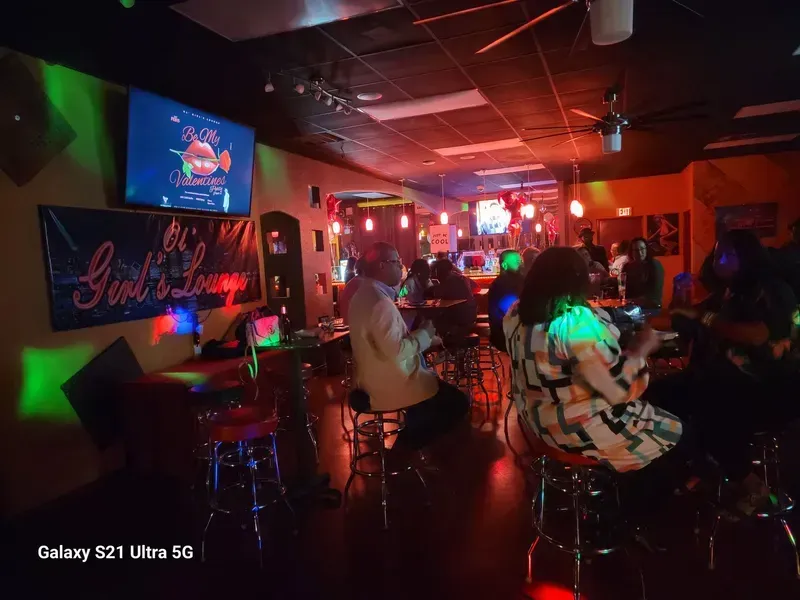 Dimly lit nightclub with people seated at tables under colorful neon lights and disco reflections
