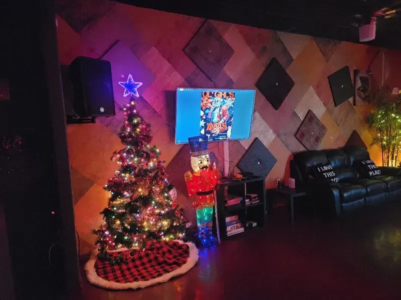 Christmas tree with colorful lights in a dim living room beside a wall-mounted TV and black couch