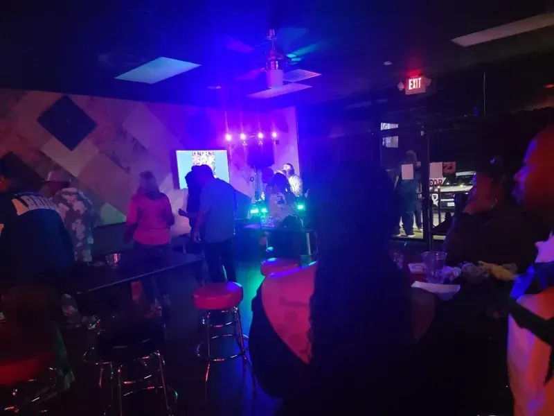 Dimly lit nightclub with people near a glowing stage and colorful purple-blue lights