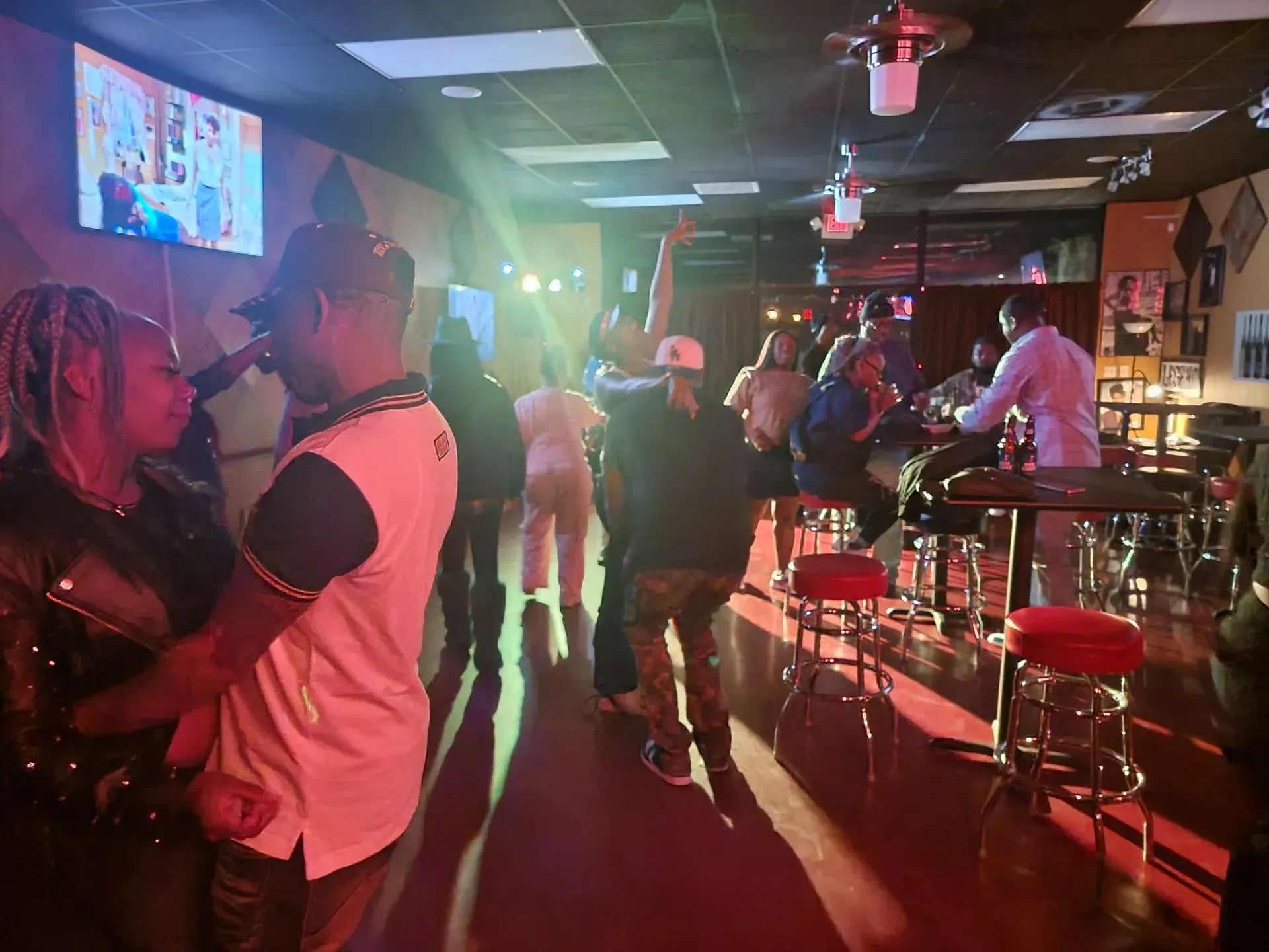 Dimly lit bar with people dancing, neon lights, and a live DJ booth