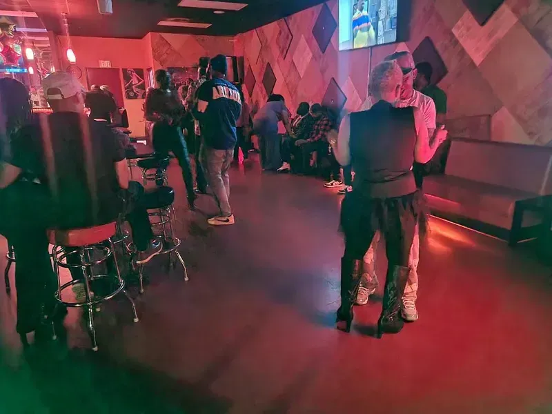 People in a red-lit lounge, standing and chatting near stools and benches.