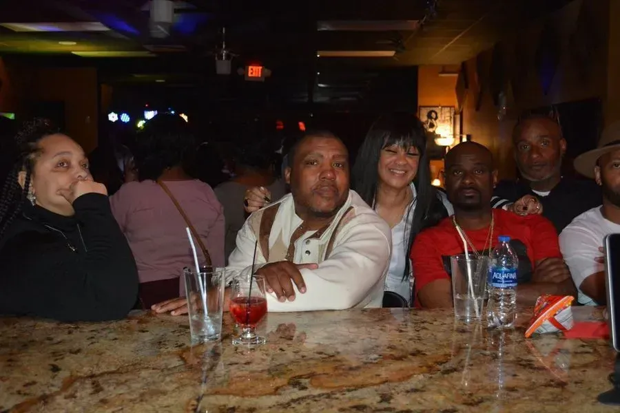 People sitting at a bar table, chatting over drinks in a dimly lit lounge.