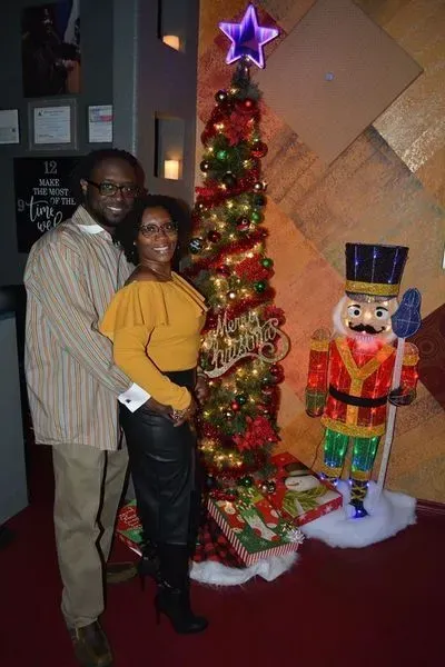 Couple posing beside a lit Christmas tree and toy soldier decoration indoors