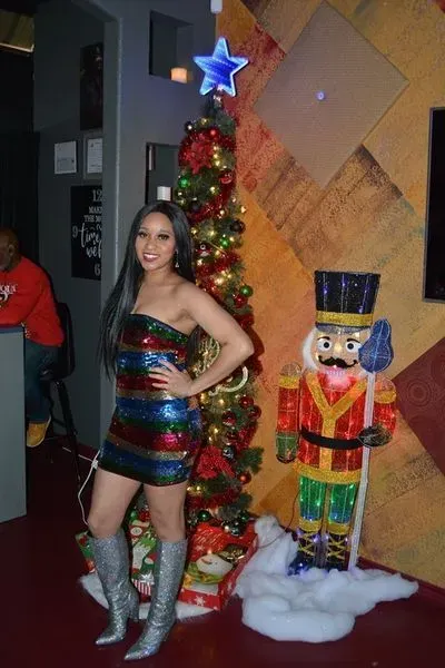 Woman in a striped dress and silver boots posing beside a lit Christmas tree and nutcracker display.