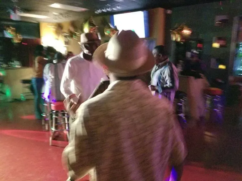 People dancing in a dimly lit room, with a person in a hat in the foreground