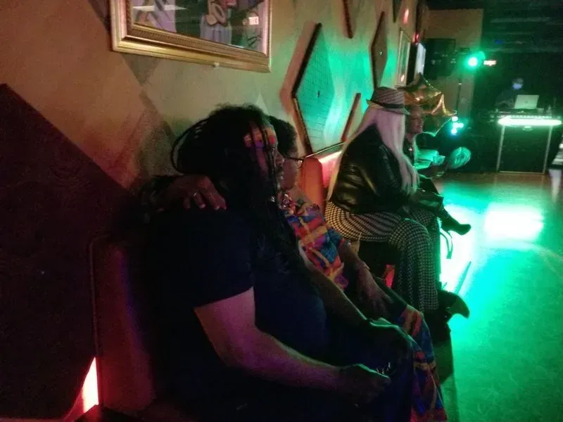 People seated along a wall in a dim nightclub with green lighting