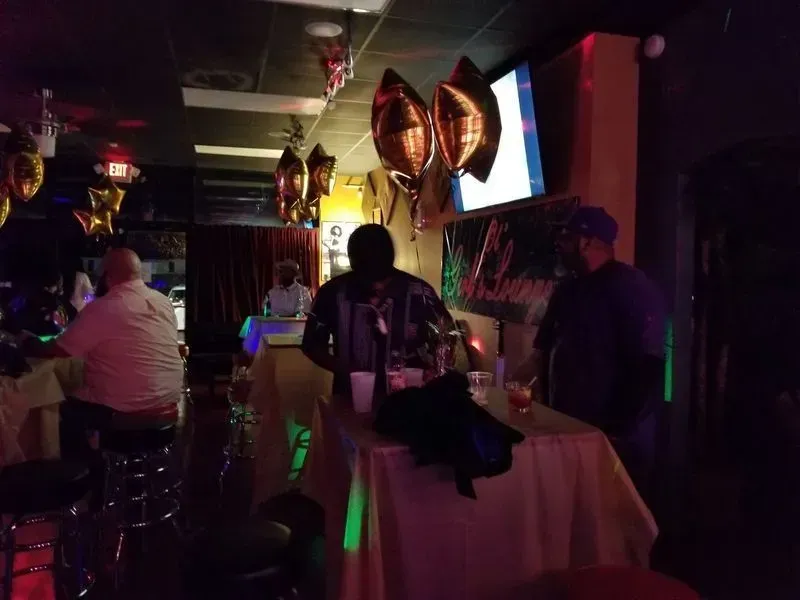 Dim bar with people seated at a counter, neon lights, and balloons in the background