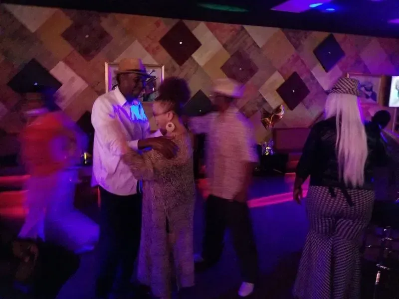 People dancing at a dimly lit party with purple lighting and a patterned wall background
