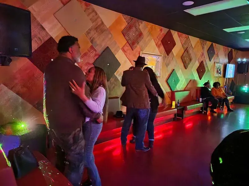 People dancing in a dimly lit club with red floor lights and patterned wall decor