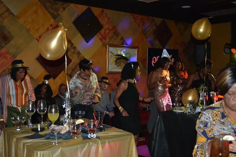 People mingling at a lively indoor party with gold balloons and decorated tables