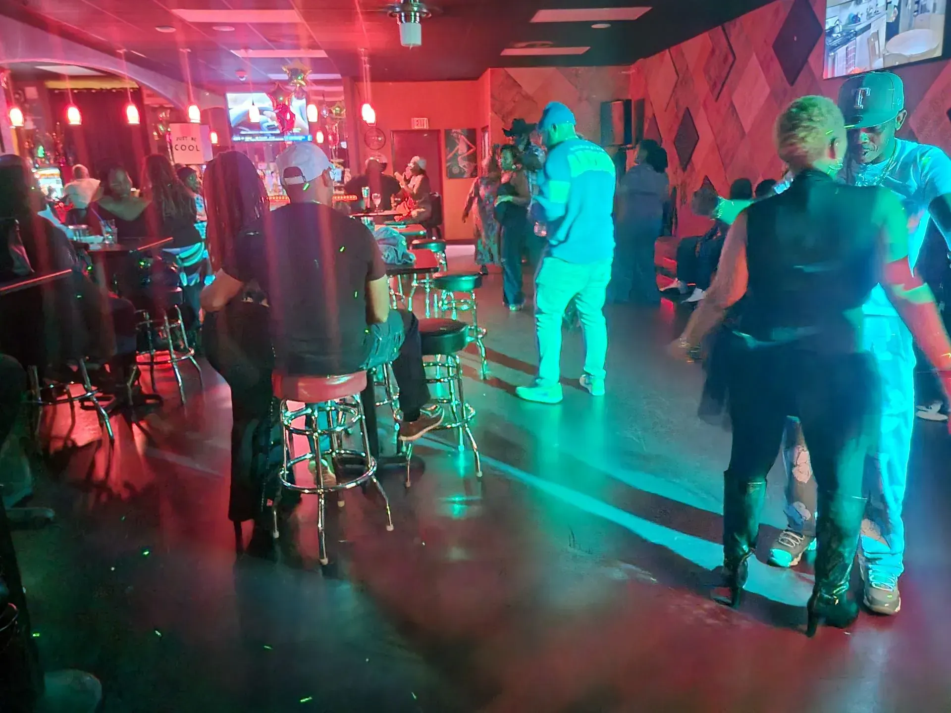 People dancing in a neon-lit nightclub with red and teal lighting and tables along the walls