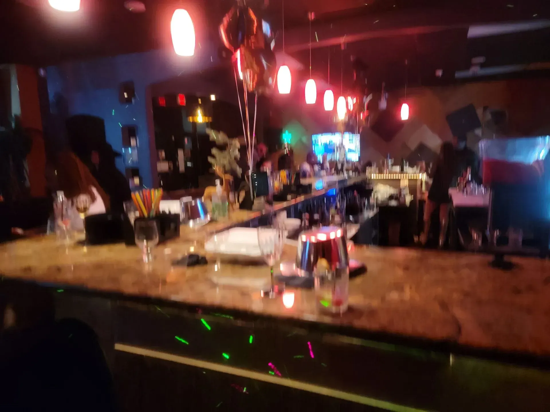 Dim bar interior with a lit counter, hanging red lights, and patrons in the background.