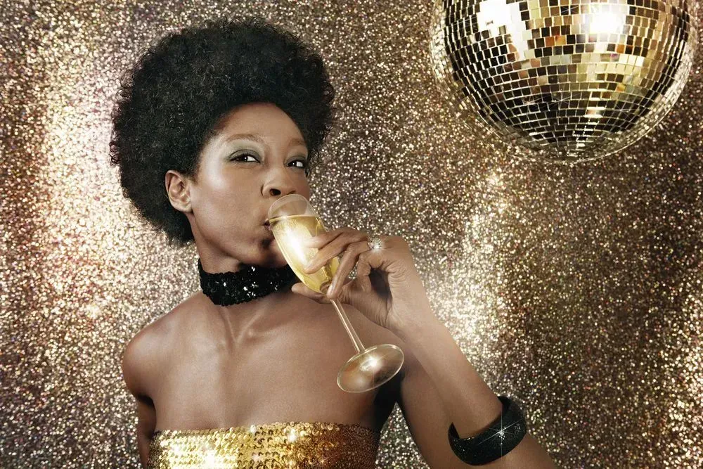 Woman in a gold dress toasting with a champagne flute against a sparkling gold backdrop