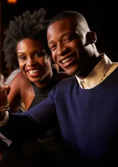 Two smiling people posing closely together against a dark background.