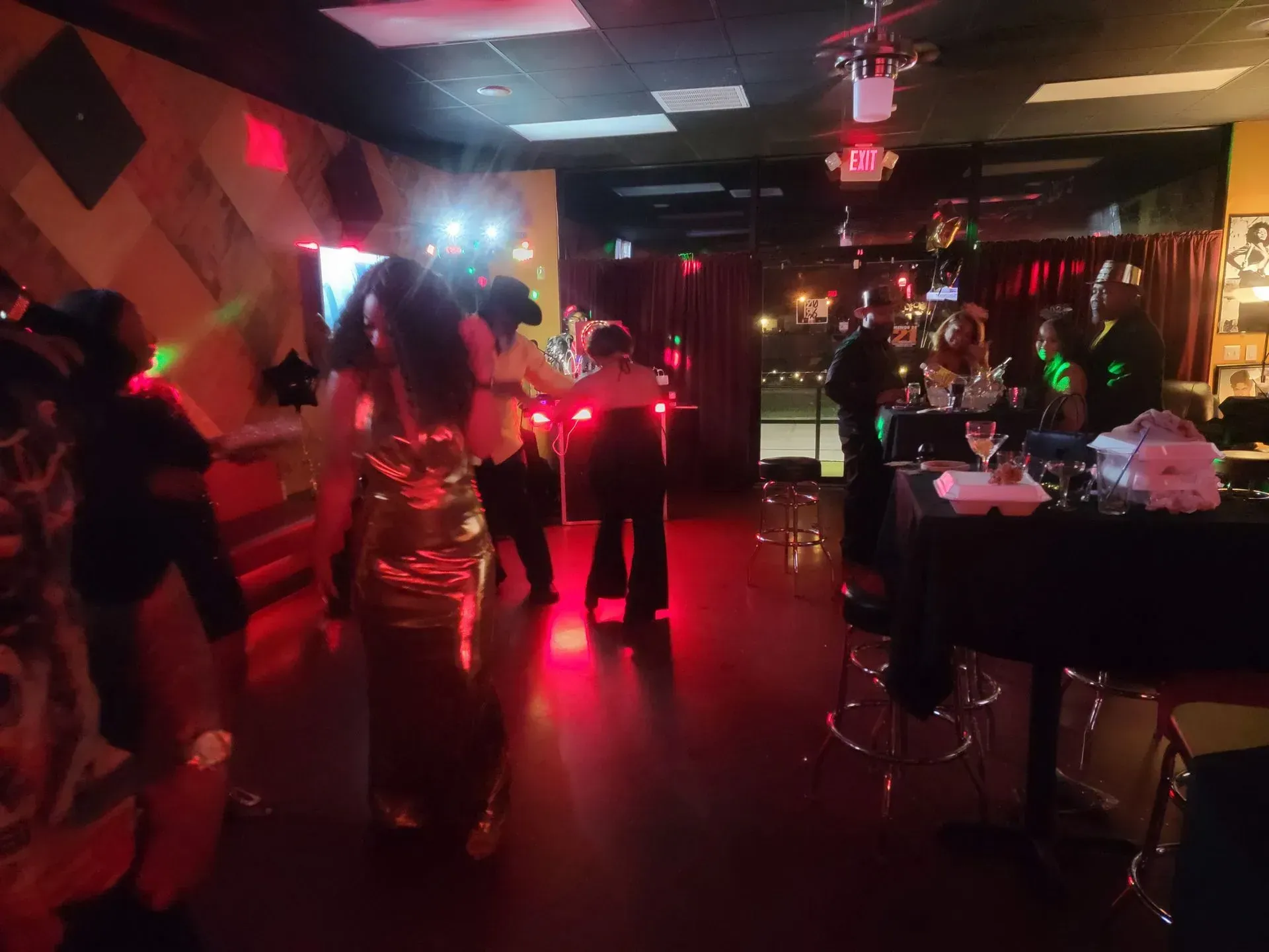 Dim nightclub with people dancing under red lights and tables along the side.