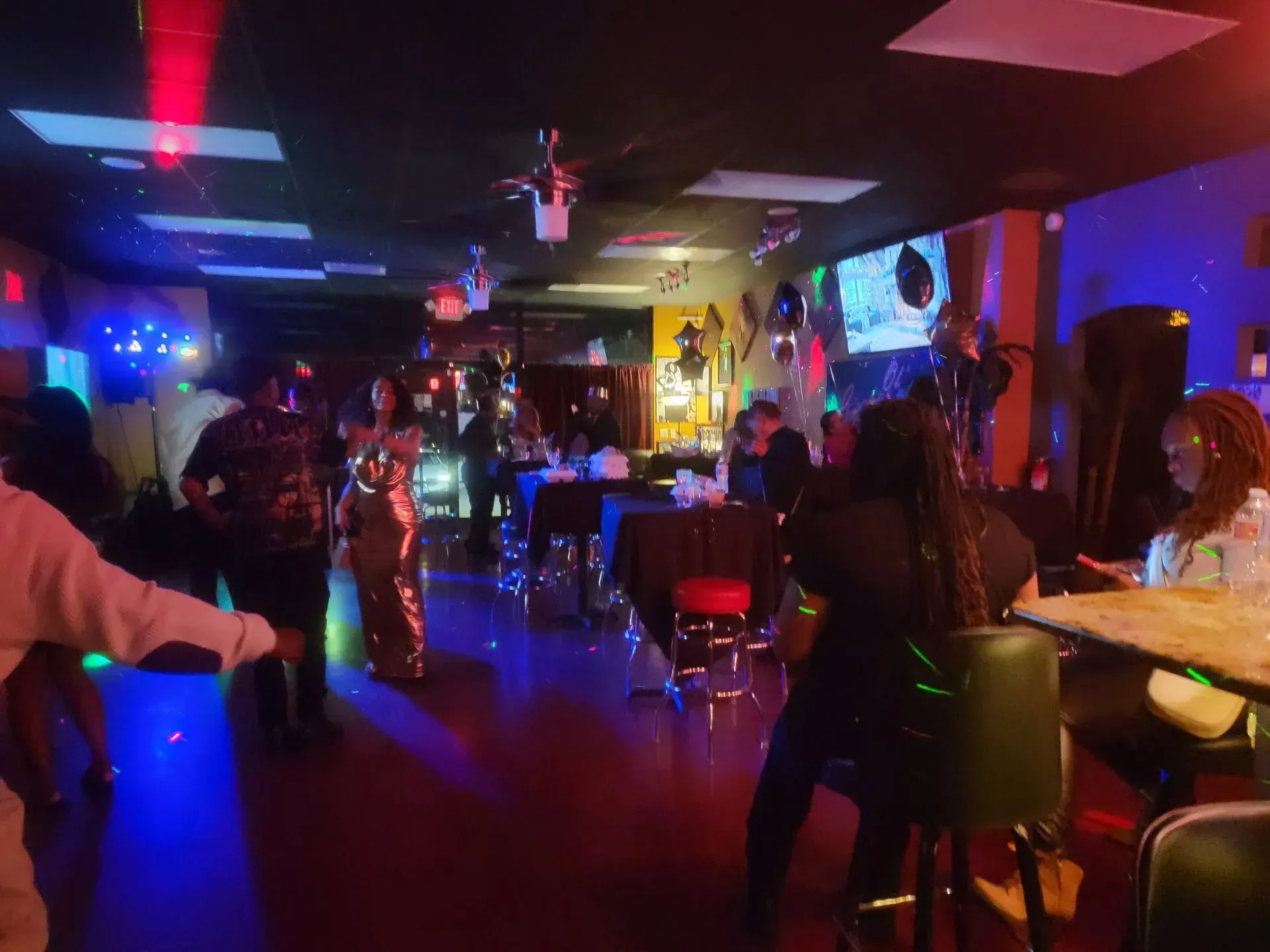 Dimly lit nightclub with people seated at tables and dancing under blue and purple lights