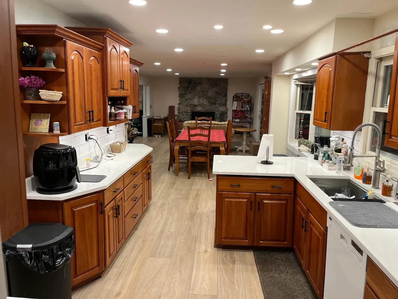 Bright kitchen with wood cabinets, white counters, and a dining table in the background.