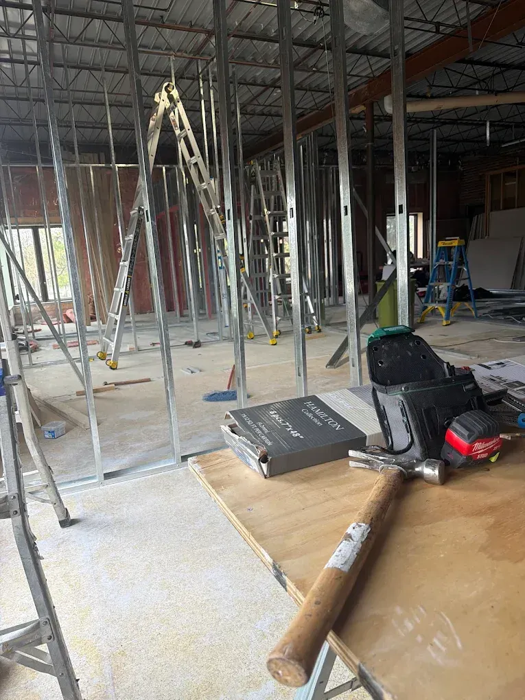 Construction site interior with metal framing, ladders, tools, and debris on the floor