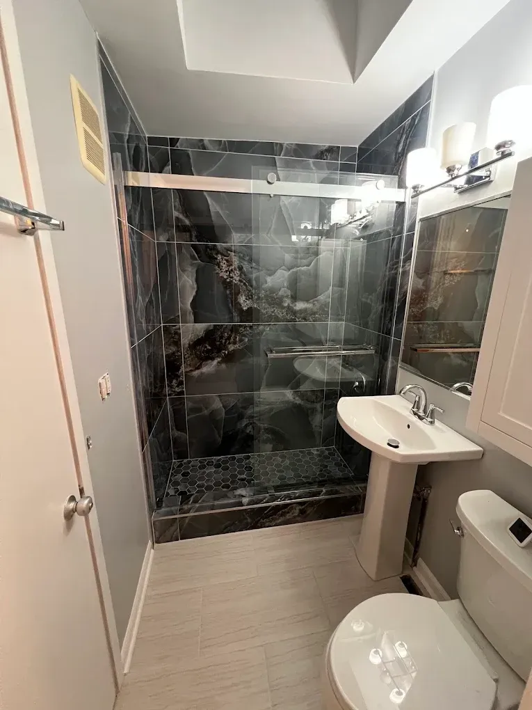 Small bathroom with sink and toilet, featuring a marble-patterned tiled shower at the back.